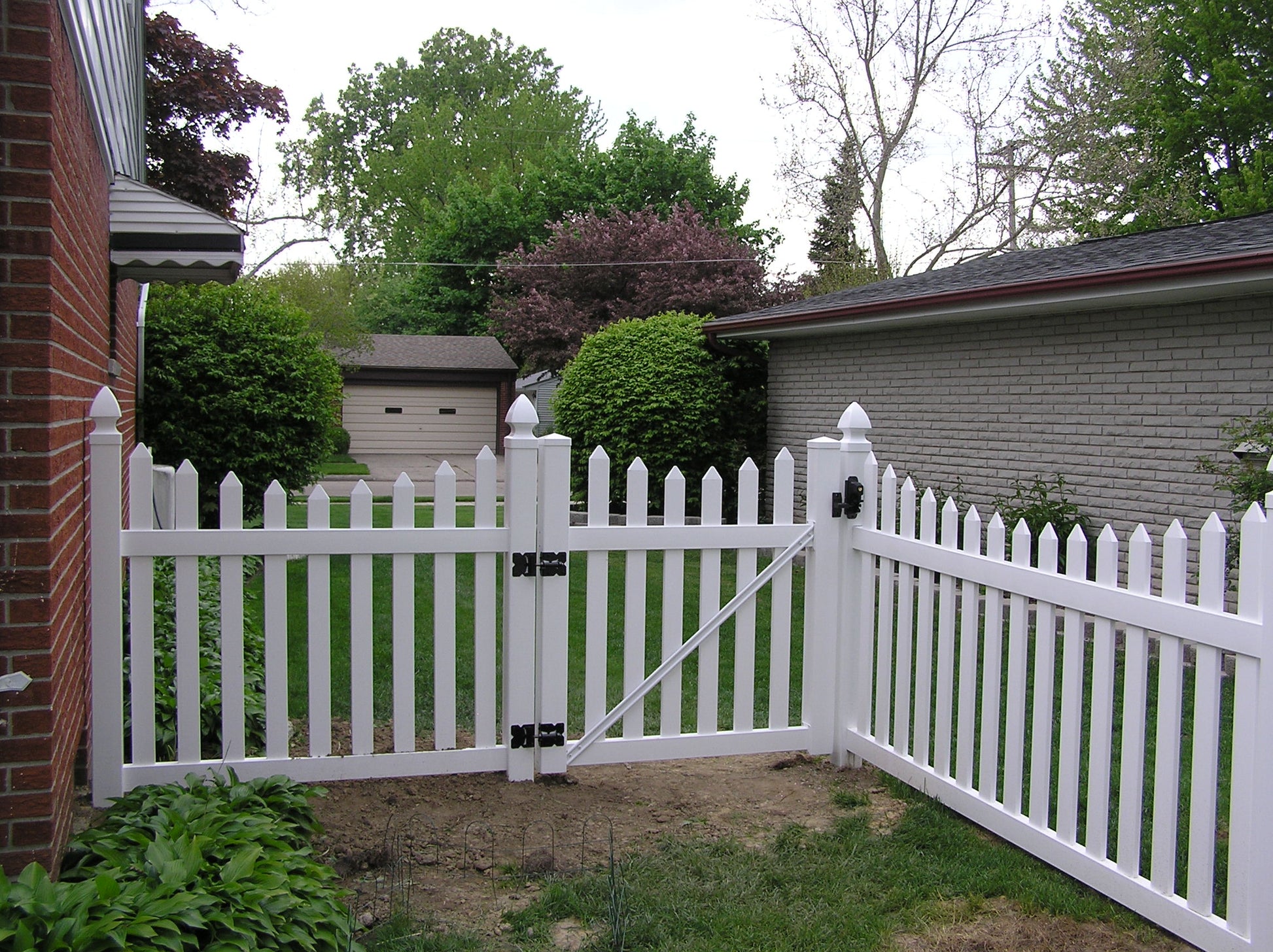 Weatherables Ellington white vinyl picket fence with a gate in front of a house with trees in the background