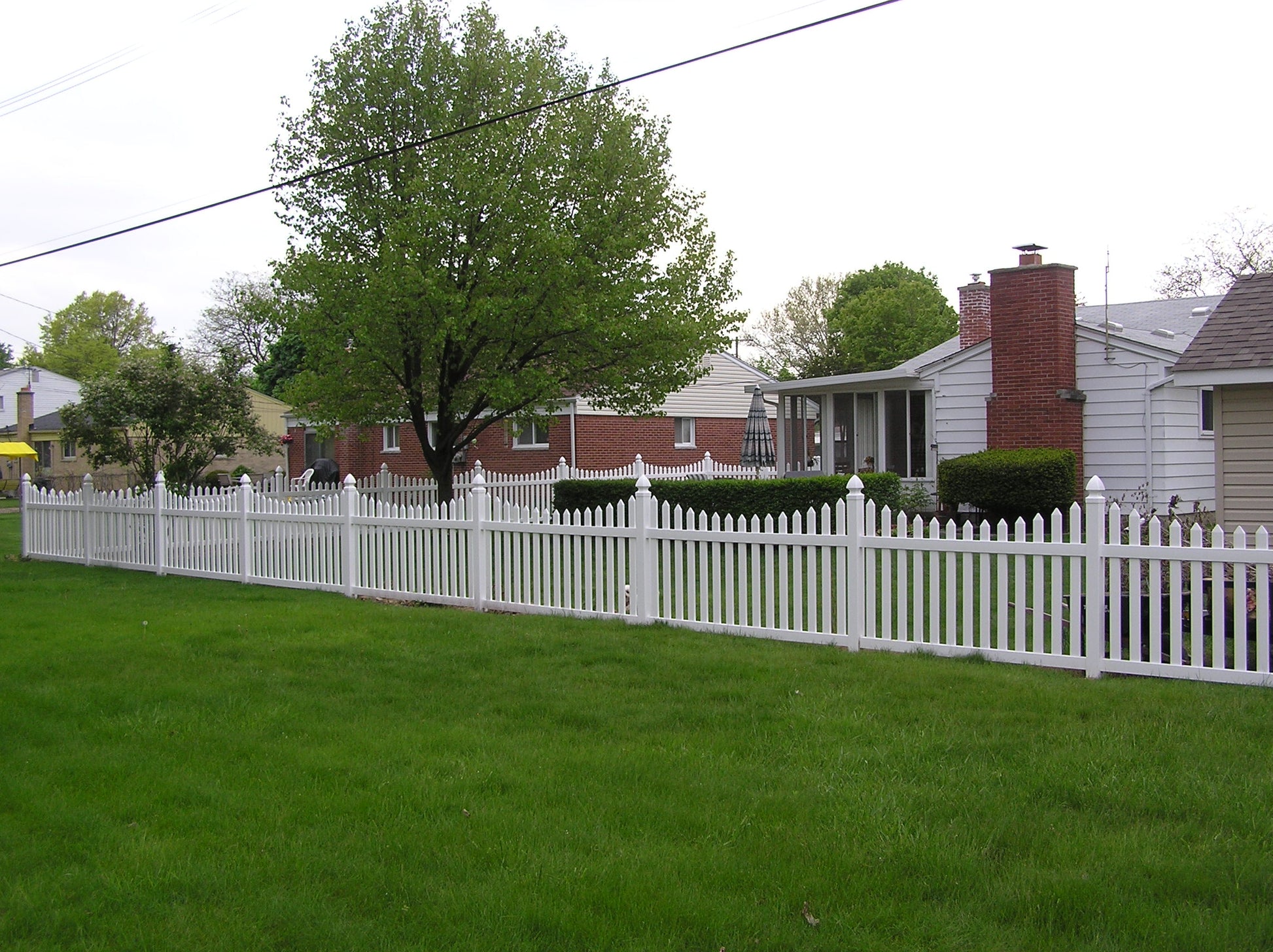 Weatherables Ellington white vinyl picket fence in front of a residential house with green grass and trees.