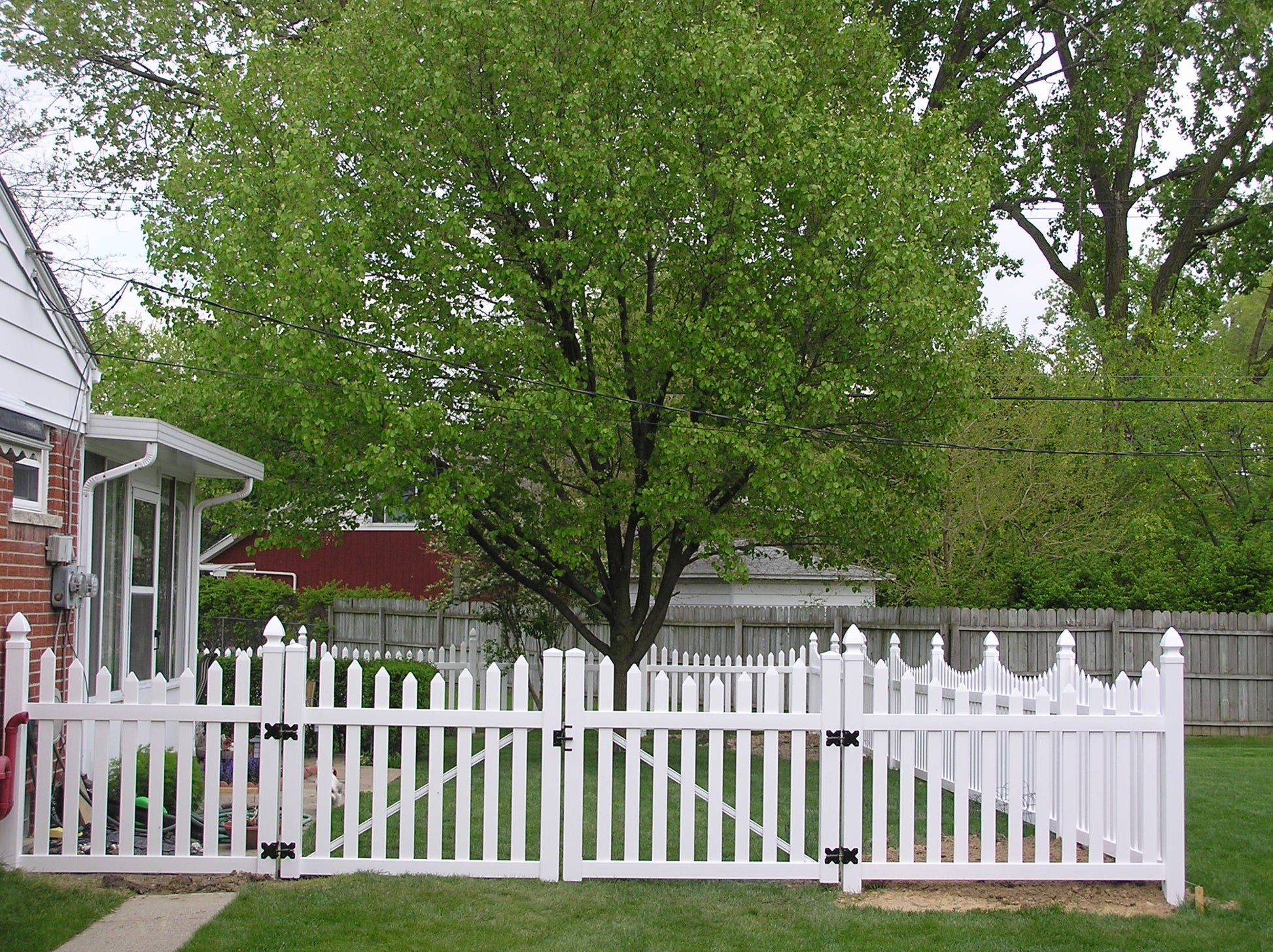 Weatherables Ellington white vinyl picket fence in a residential area with trees and houses in the background.