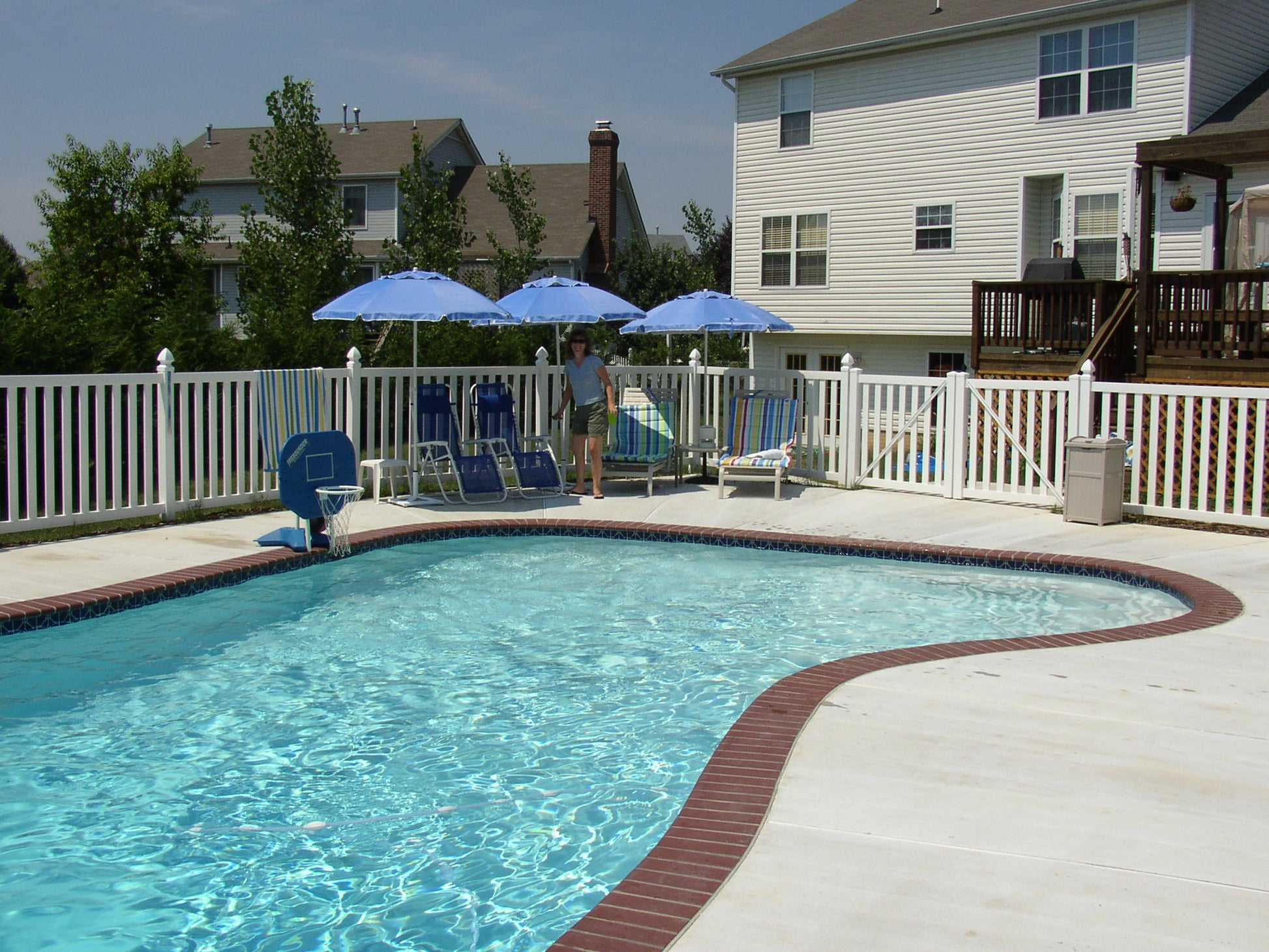 Pool area with lounge chairs, umbrellas, Weatherables Captiva white vinyl closed-top picket fence and a house in the background