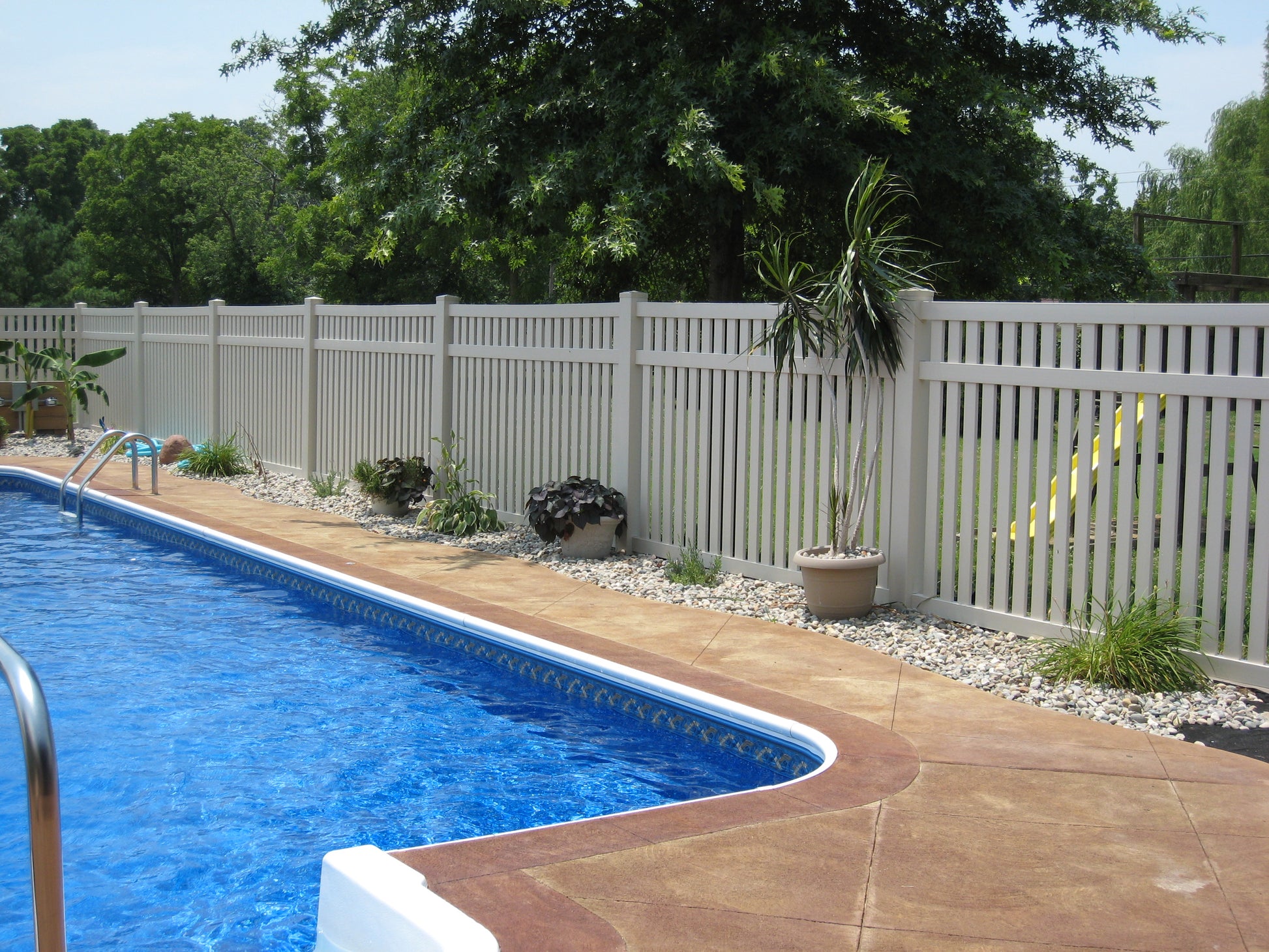 Swimming pool with a Weatherables Crestview white vinyl fence and trees in the background