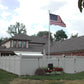 House with a Weatherables Ashton white vinyl privacy fence, American flag, and garden in front of a blue sky.