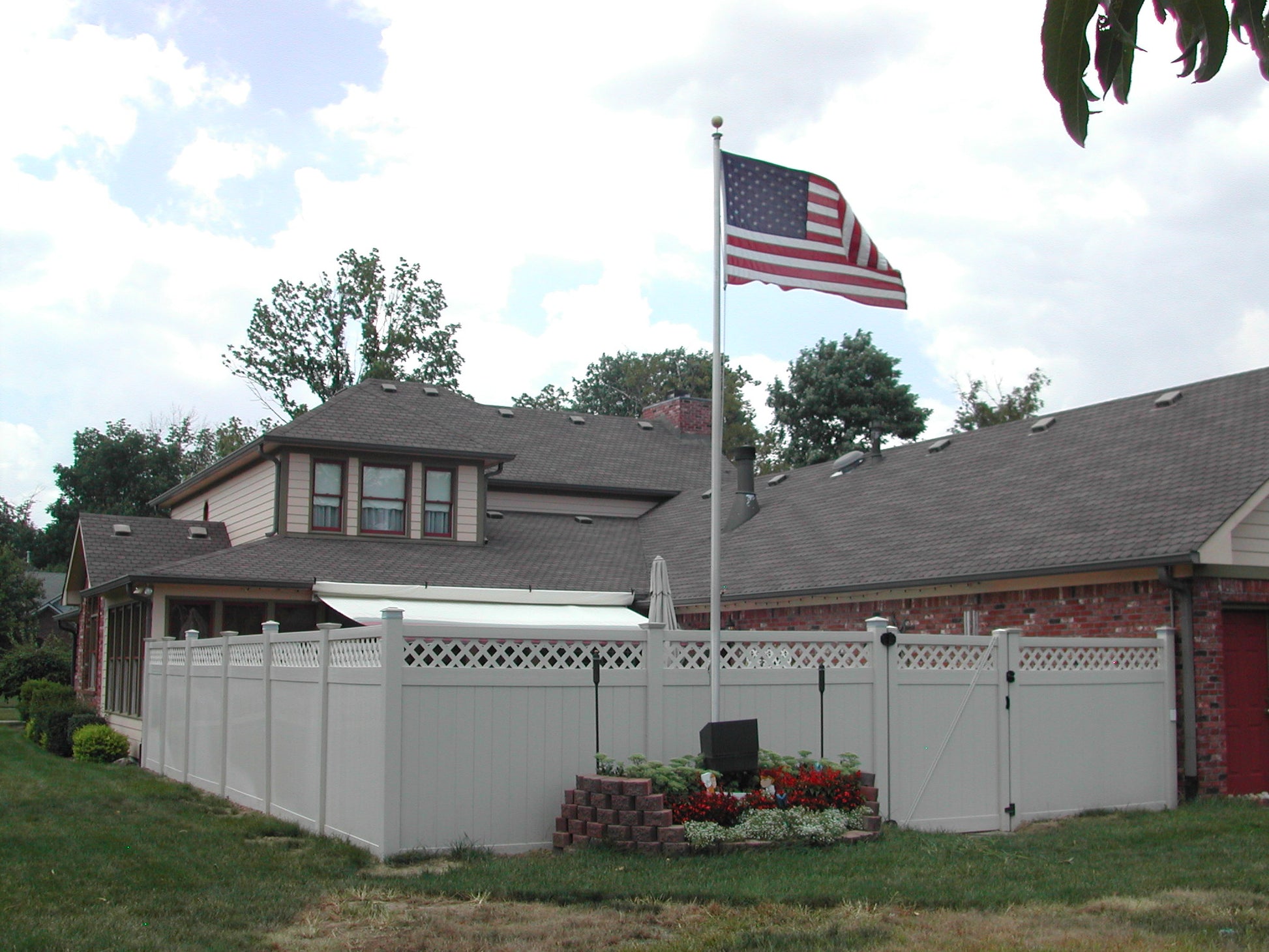 House with a Weatherables Ashton white vinyl privacy fence, American flag, and garden in front of a blue sky.