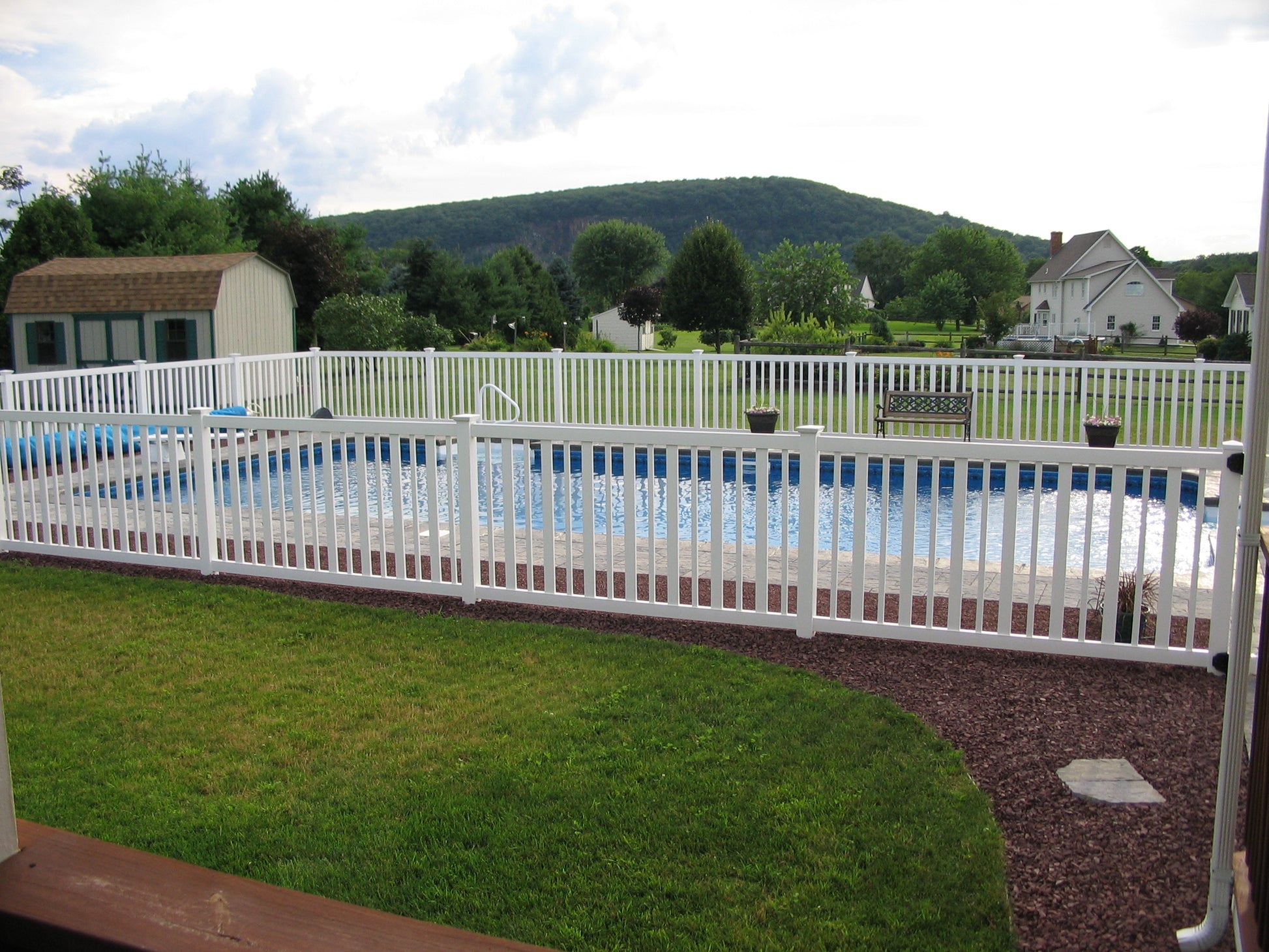 Pool area with Weatherables Atlantis white vinyl pool fence, grass, and distant mountains