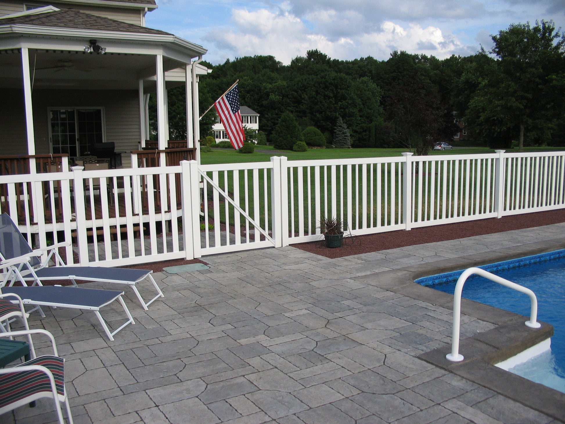 Outdoor patio area with pool, chairs, and a Weatherables Atlantis white vinyl closed-top picket fence.