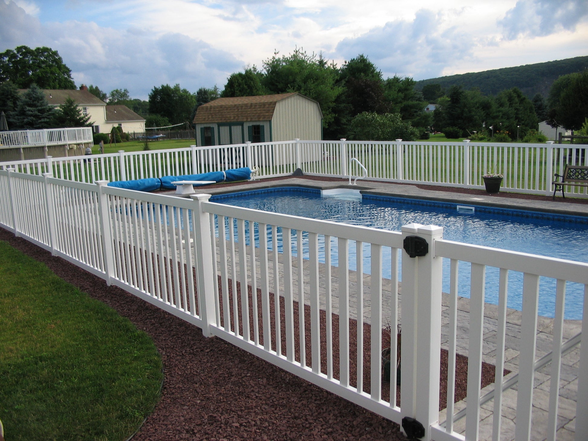Pool area with Weatherables Atlantis white vinyl pool fence, lounge chairs, and surrounding greenery.