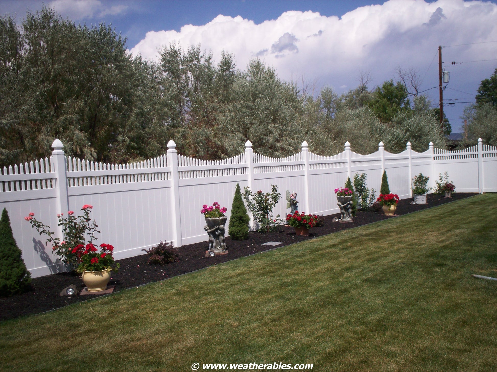 Weatherables Halifax white vinyl privacy fence with decorative plants and flowers in a well-maintained garden.