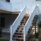Weatherables Washington white vinyl deck railing on a wooden staircase leading to a deck on a house with outdoor furniture and tools.