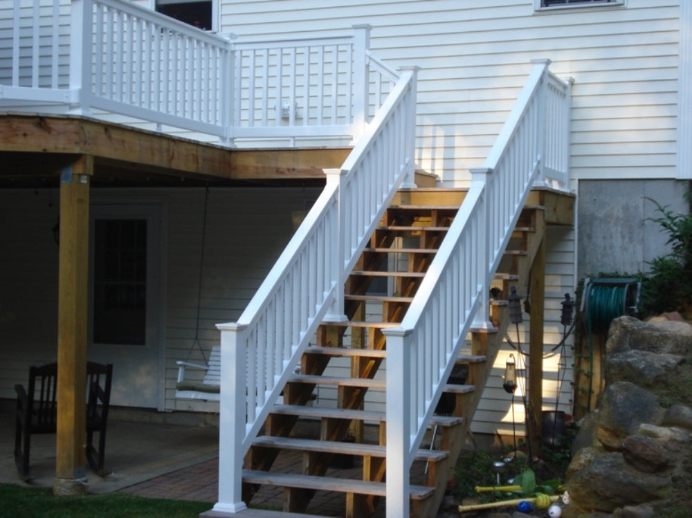 Weatherables Washington white vinyl deck railing on a wooden staircase leading to a deck on a house with outdoor furniture and tools.