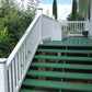 Green wooden steps leading to a  deck with Weatherables Washington white vinyl deck railing, surrounded by greenery.