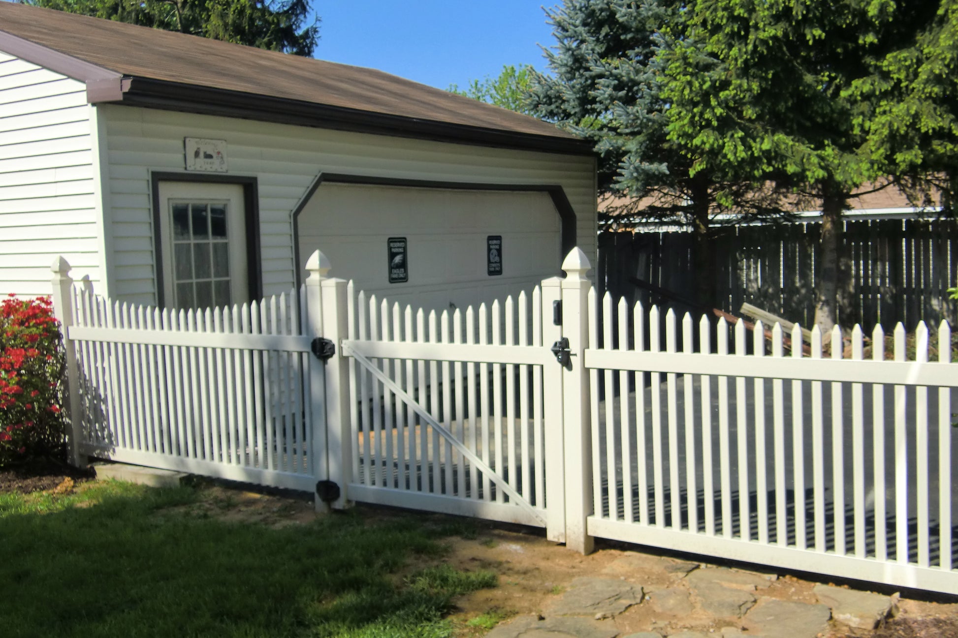 Weatherables Barrington white vinyl picket fence in front of a house with trees and blue sky in the background
