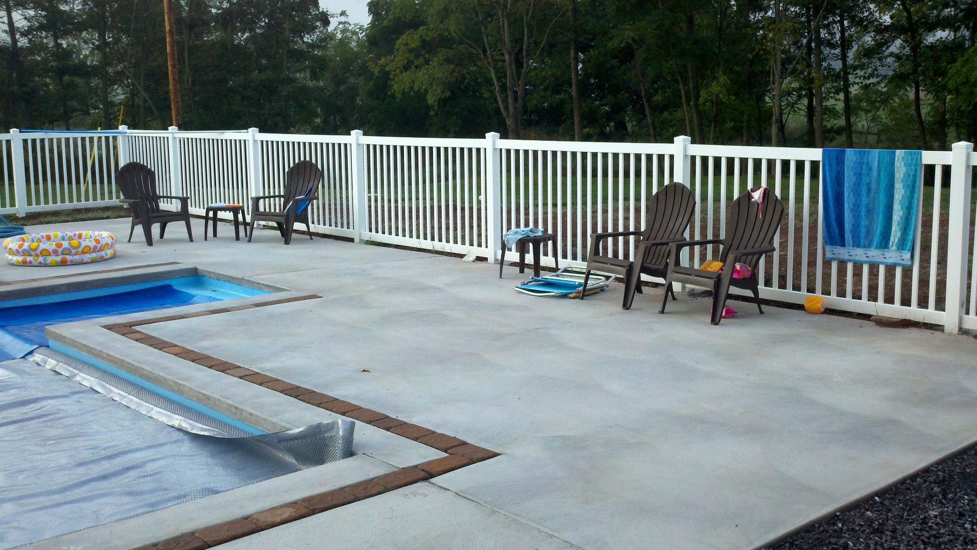 Pool area with Adirondack chairs, a towel, and pool toys on a deck with Weatherables Neptune white vinyl pool fence
