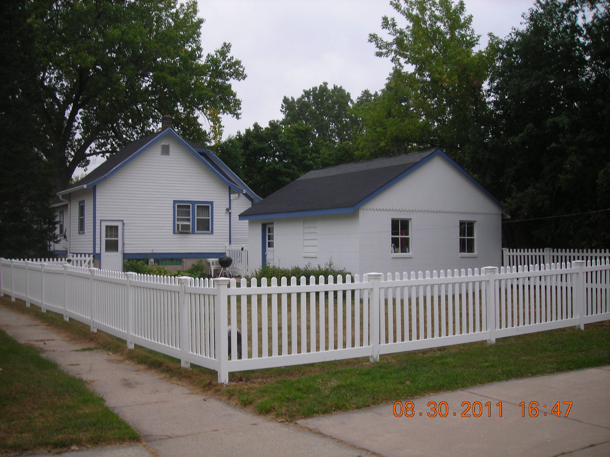 Two small houses with a Weatherables Plymouth white vinyl picket fence and trees in the background.