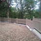 Paved area with a Weatherables Chelsea khaki vinyl picket fence and trees in the background