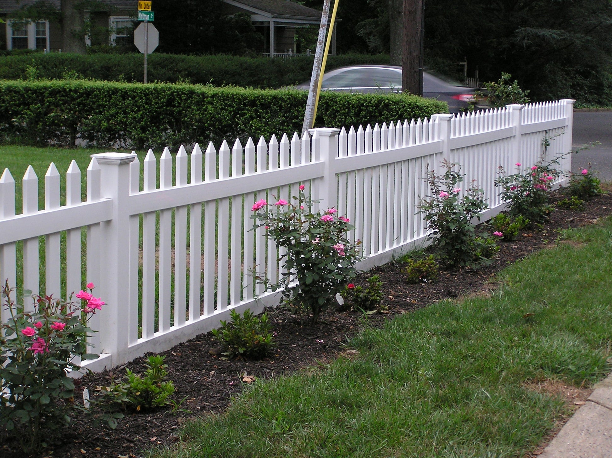 Weatherables Chelsea white vinyl picket fence with flowering bushes and a house in the background