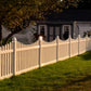 Weatherables Hampshire tan vinyl picket fence in front of a house with trees and grass.