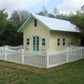 Small yellow house with a Weatherables Hampshire white vinyl picket fence surrounded by trees