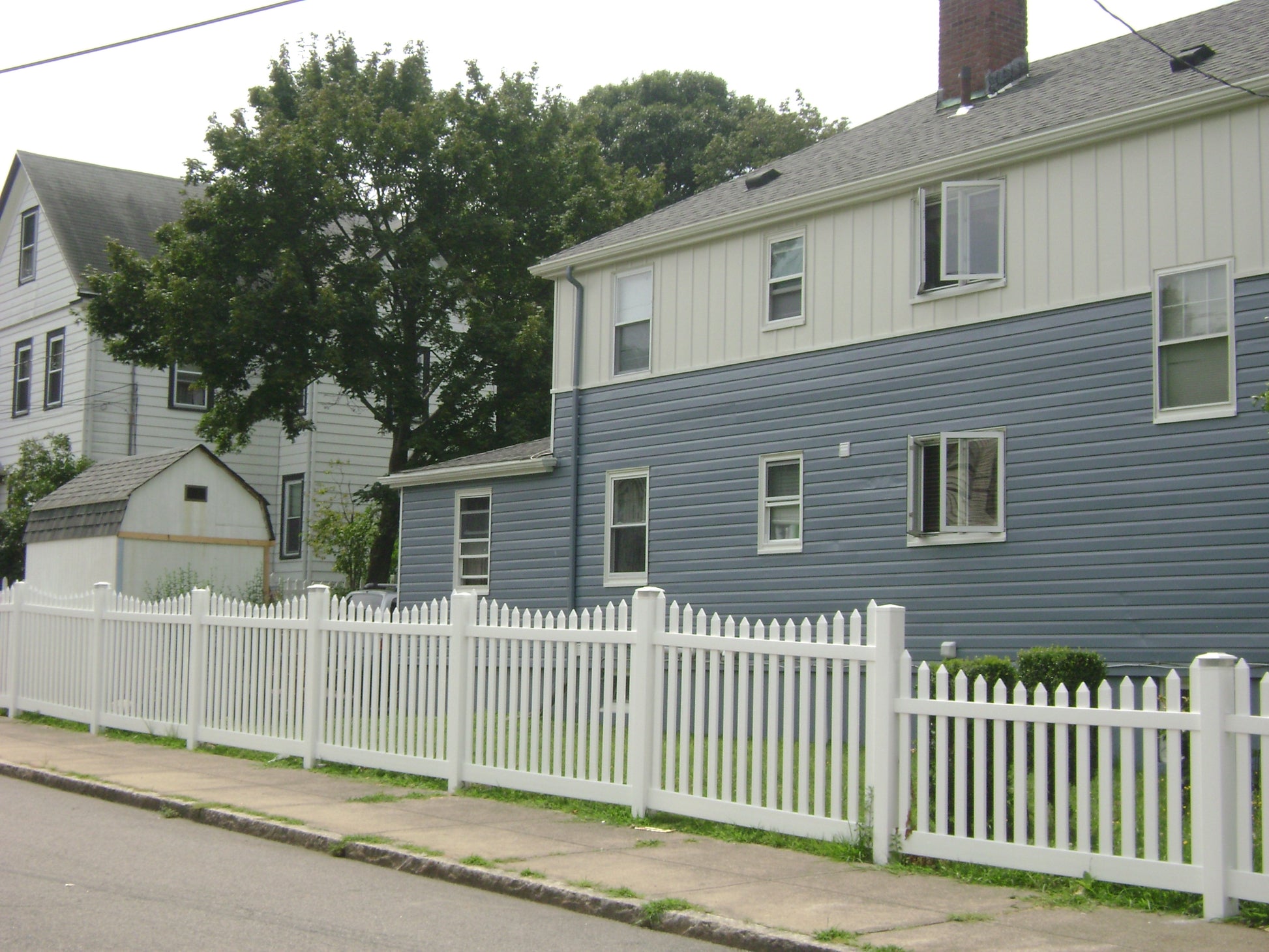 Two residential houses with a Weatherables Hampshire white vinyl picket fence in the foreground.