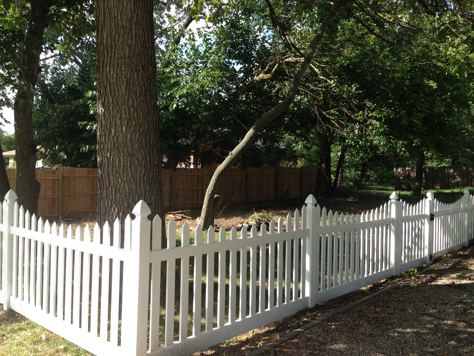 Weatherables Hampshire white vinyl picket fence with trees and a wooden fence in the background