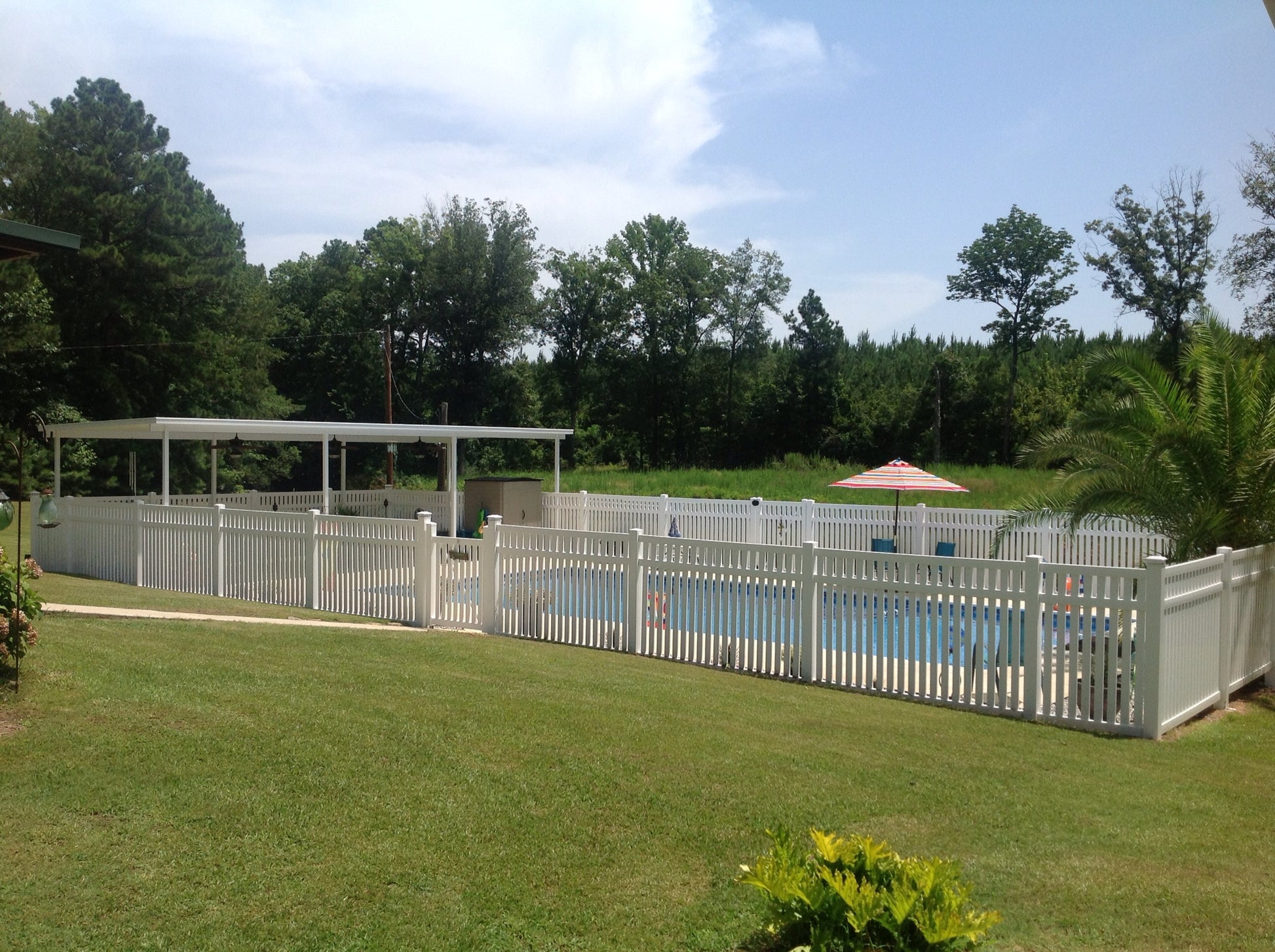 Backyard with pool, Weatherables Captiva white vinyl pool fence, and trees under a blue sky.