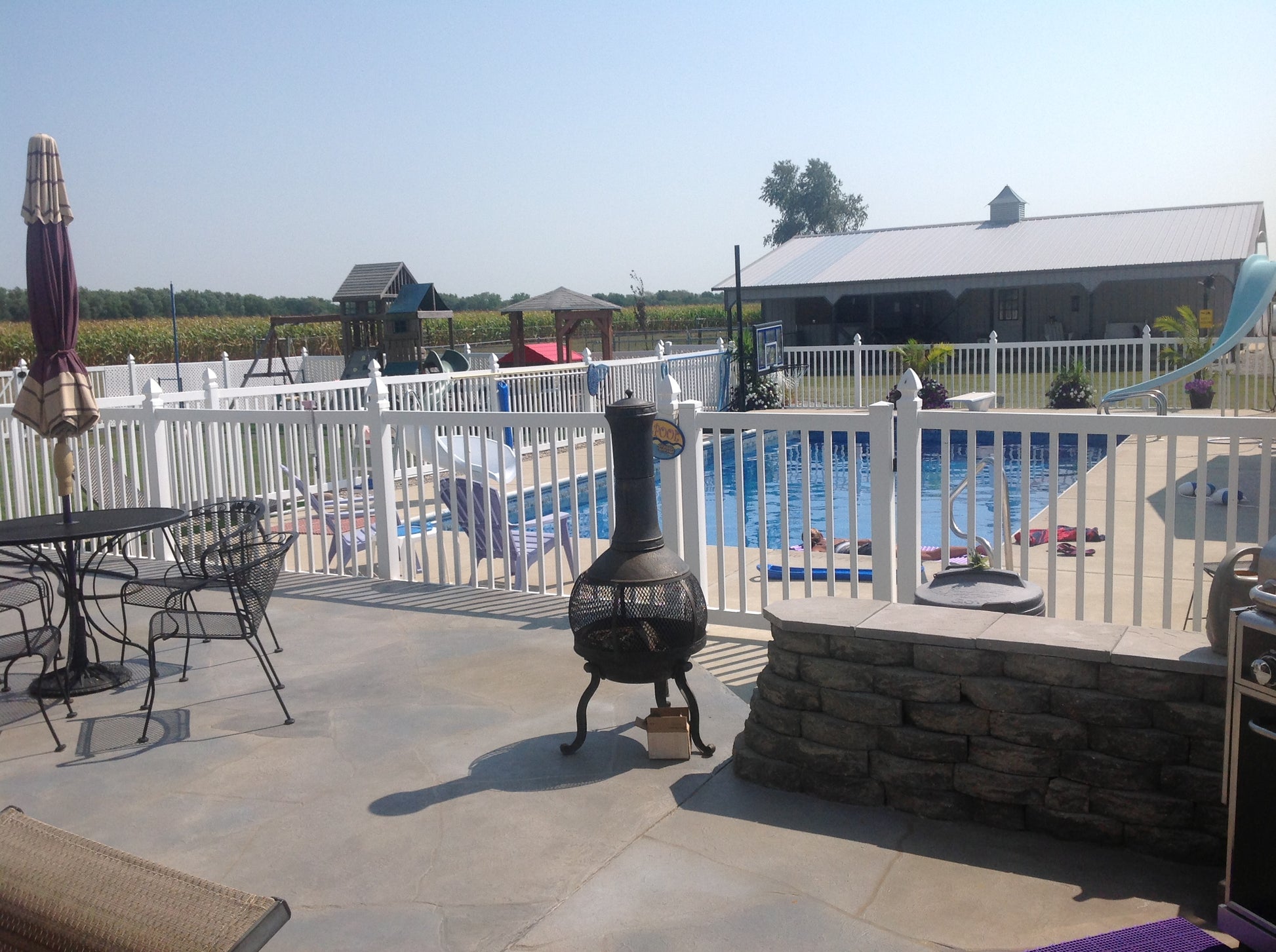 Outdoor patio area with pool, chairs, and a fire pit surrounded by Weatherables Neptune white vinyl pool fencing