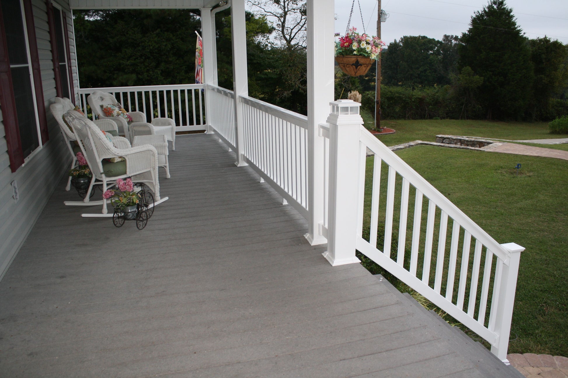 Front porch with Weatherables Washington white vinyl deck railing, chairs, and a small table with flowers on a grassy area.