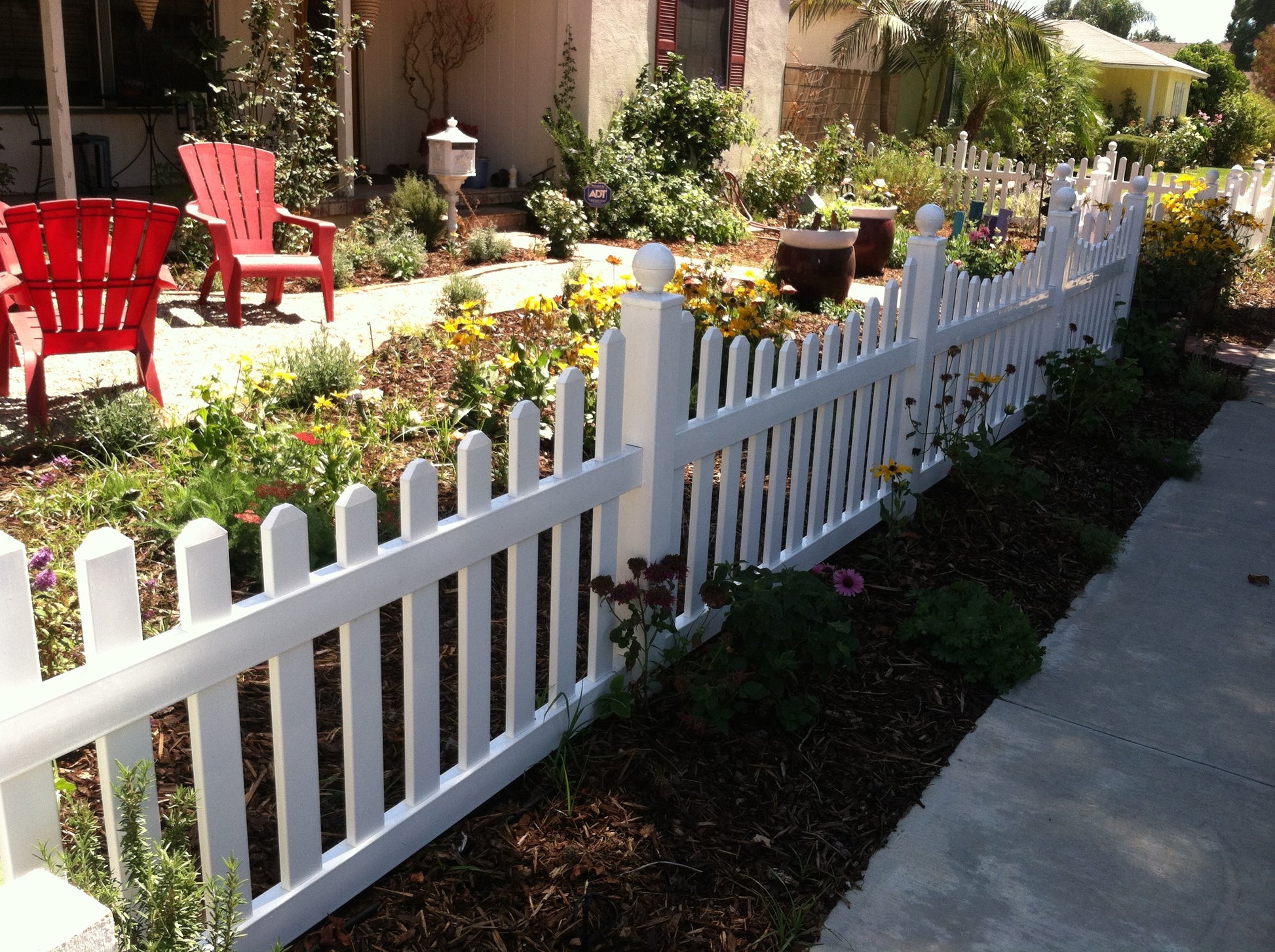 Weatherables Ellington white vinyl picket fence with garden and red chairs in the background