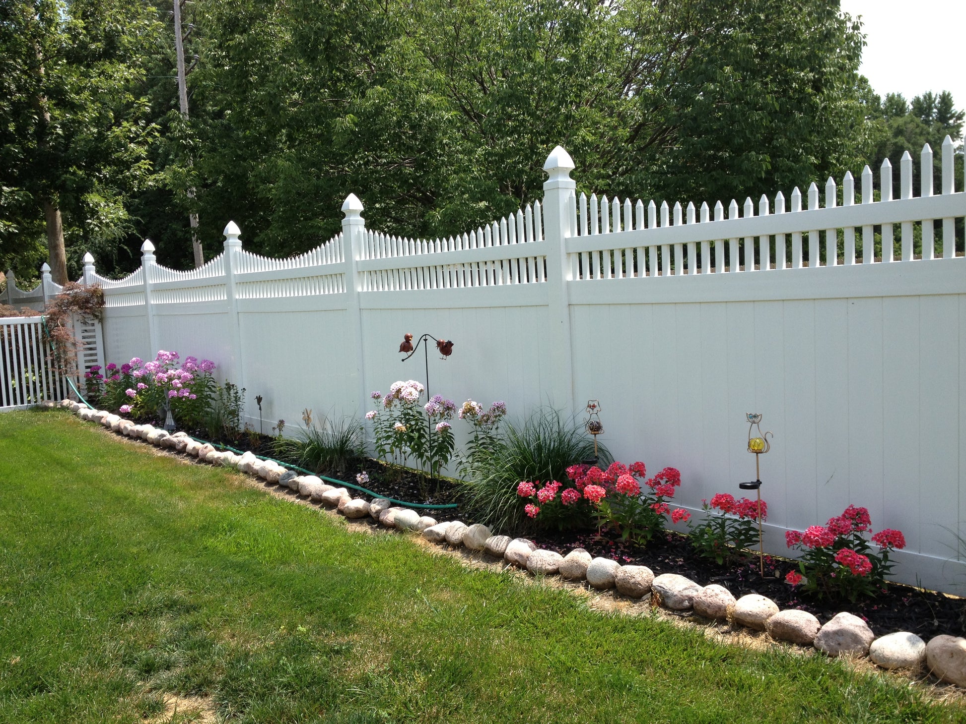 Weatherables Halifax white vinyl scallop-top privacy fence with garden and flowers in a residential setting