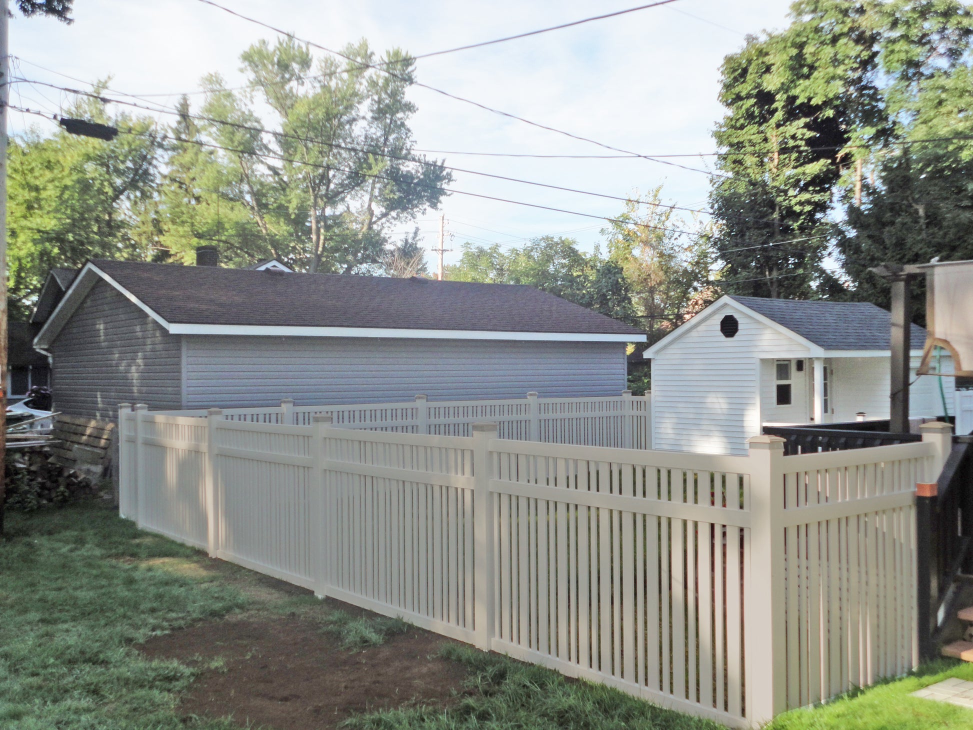 Backyard with a Weatherables Sarasota tan vinyl pool fence, grass, and trees under a clear sky.