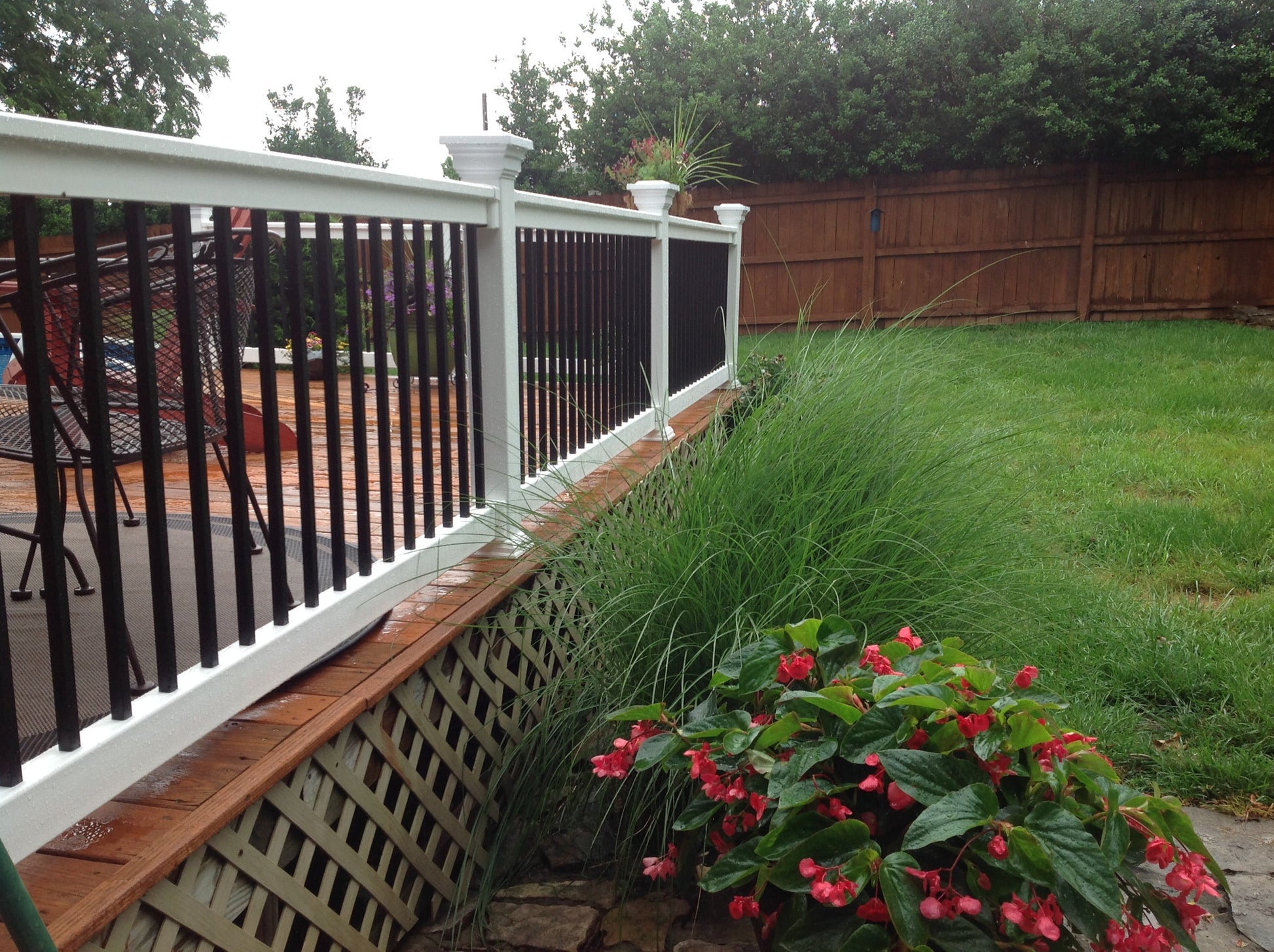 Backyard with a deck, Weatherables Birmingham white vinyl deck railing featuring black balusters, and garden with red flowers.
