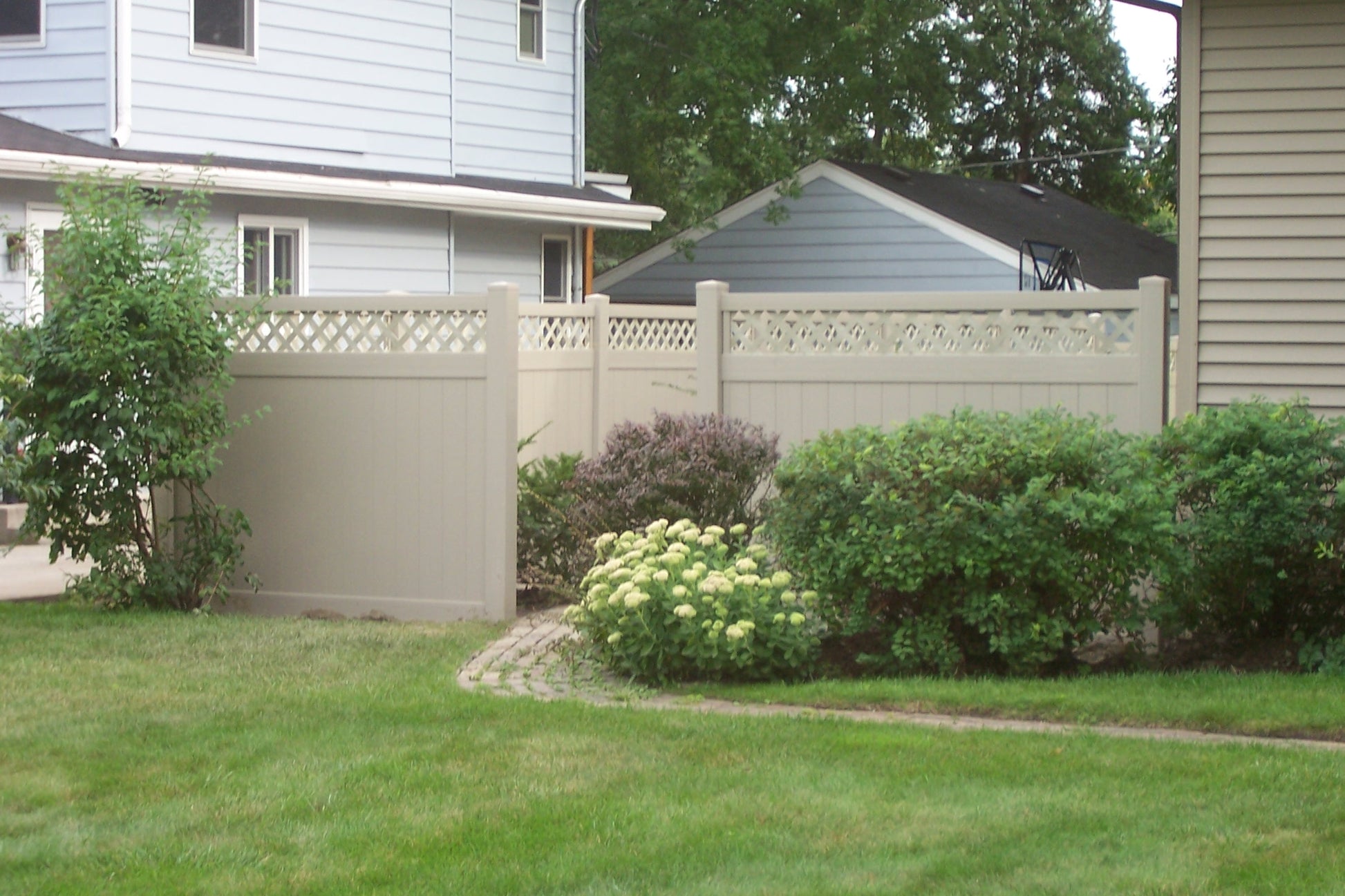 Neighborhood scene with a house, Weatherables Ashton khaki vinyl privacy fence, and greenery