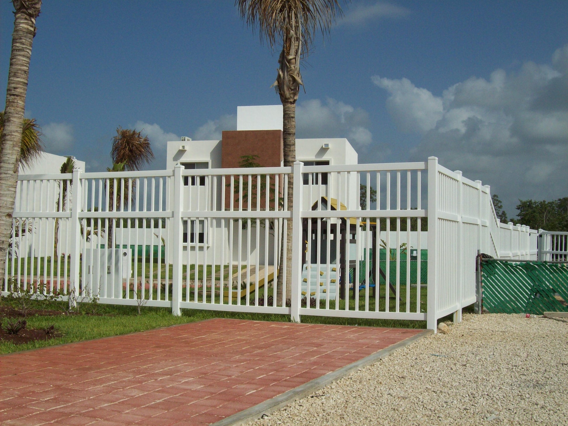 Weatherables Neptune 5 foot white vinyl pool fence with a pathway leading to a house under a blue sky.