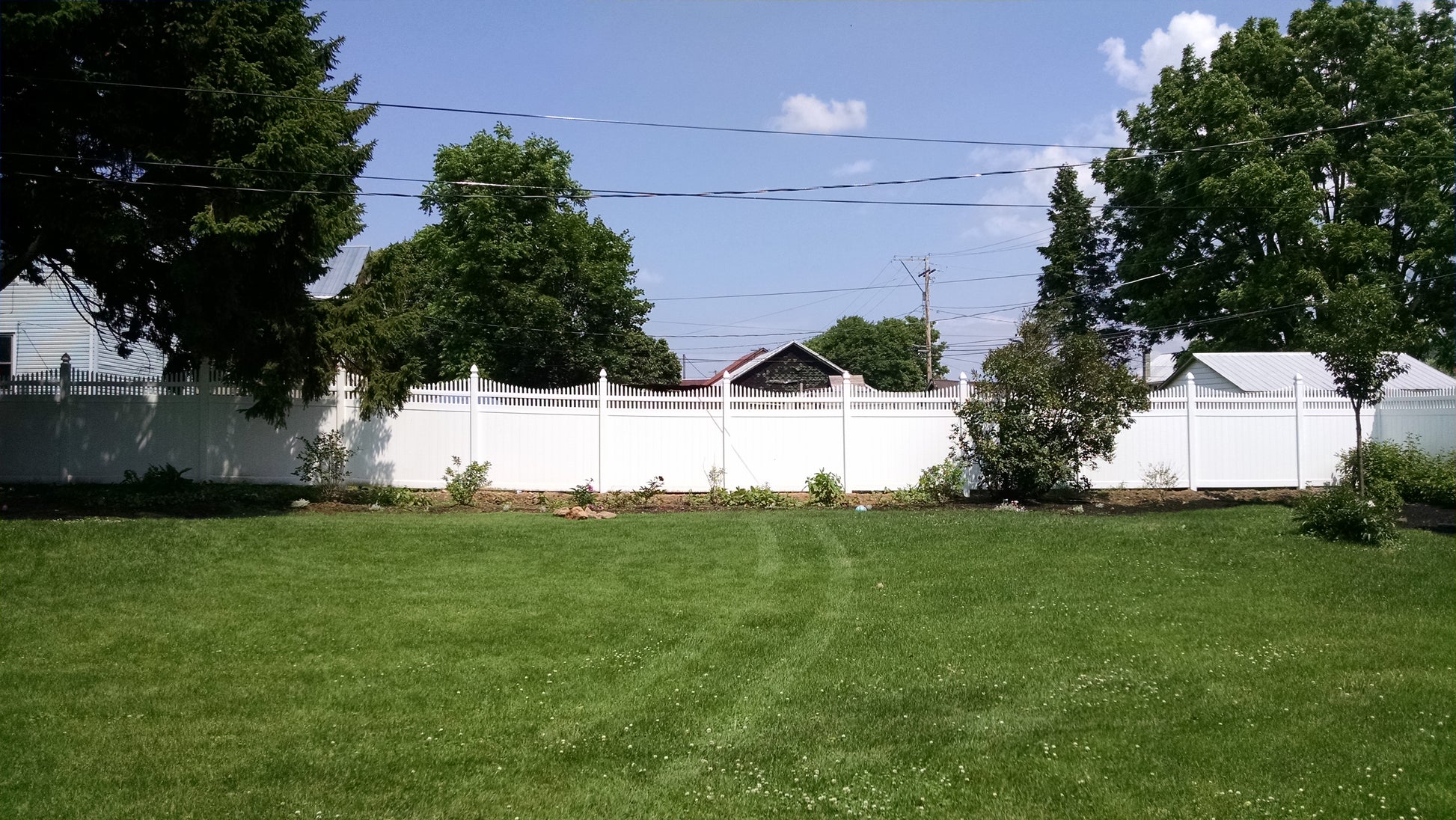 Lawn with a Weatherables Halifax white vinyl privacy fence and trees under a blue sky