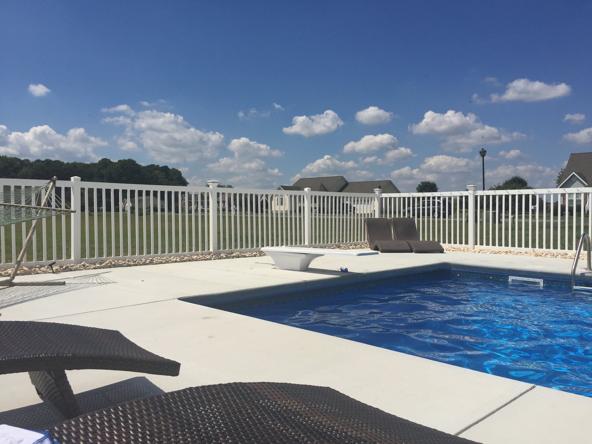 Pool area with lounge chairs and a Weatherables white vinyl pool fence under a blue sky.