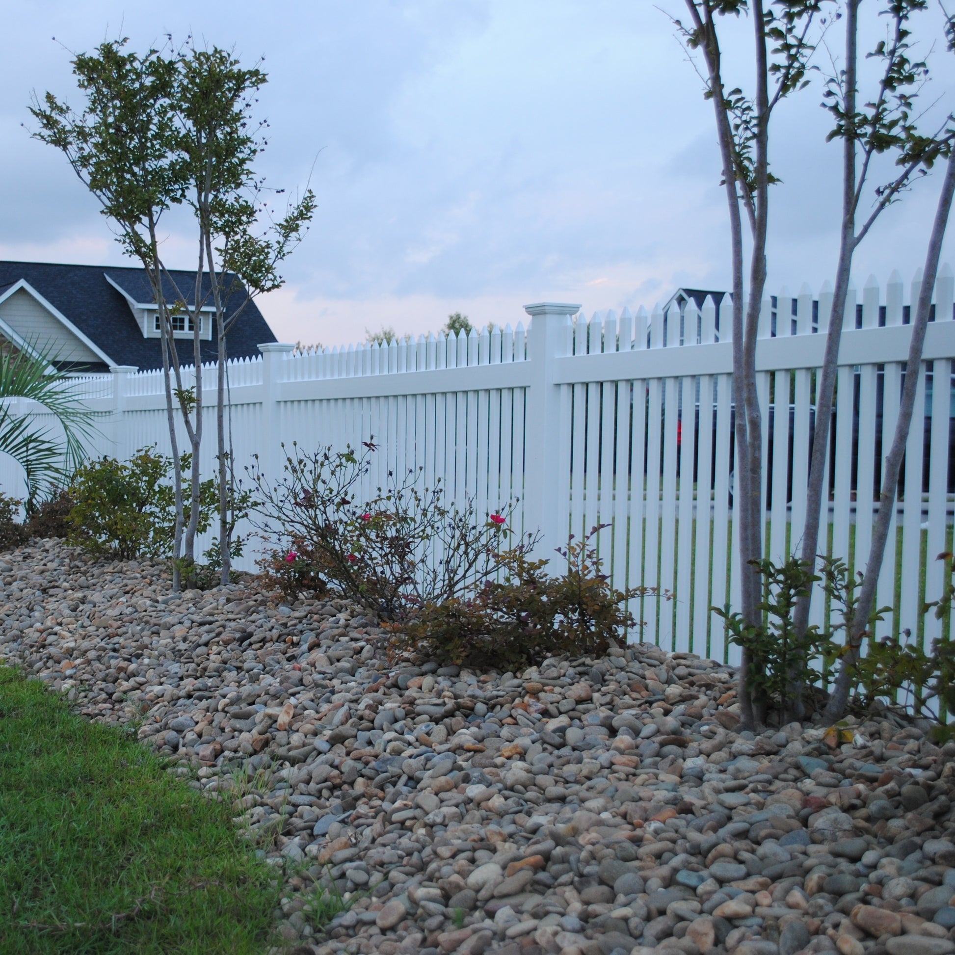 Lawn with rocks, small trees, and a Weatherables Hartford white vinyl picket fence.