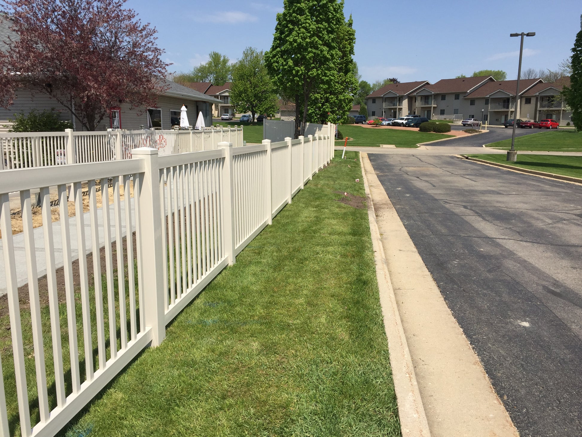 Neighborhood street with a Weatherables Neptune white vinyl pool fence and green grass