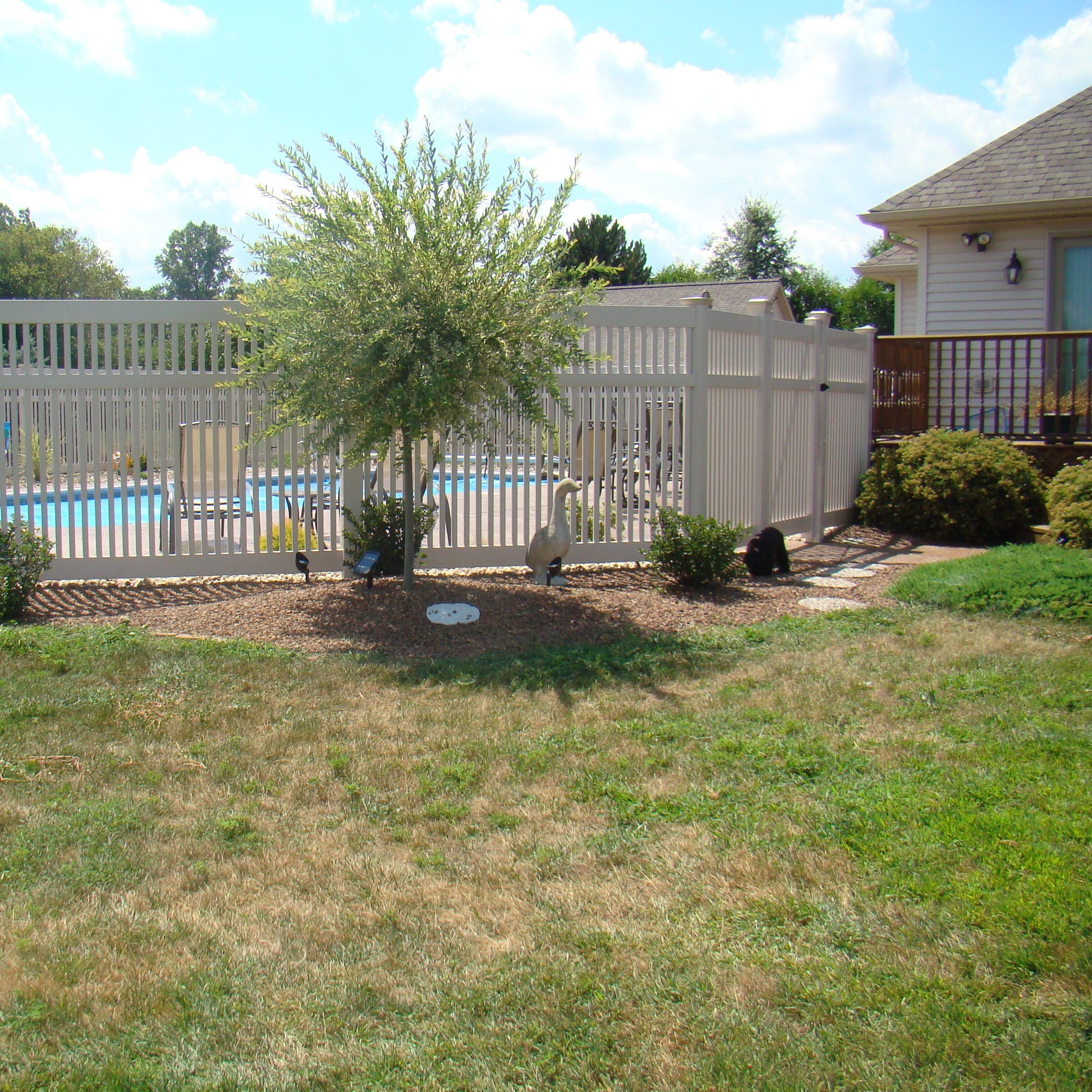 Backyard with pool, Weatherables Neptune tan vinyl pool fence, and trees on a sunny day