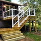Wooden deck with Weatherables Birmingham white vinyl stair railings leading to a house, surrounded by greenery.