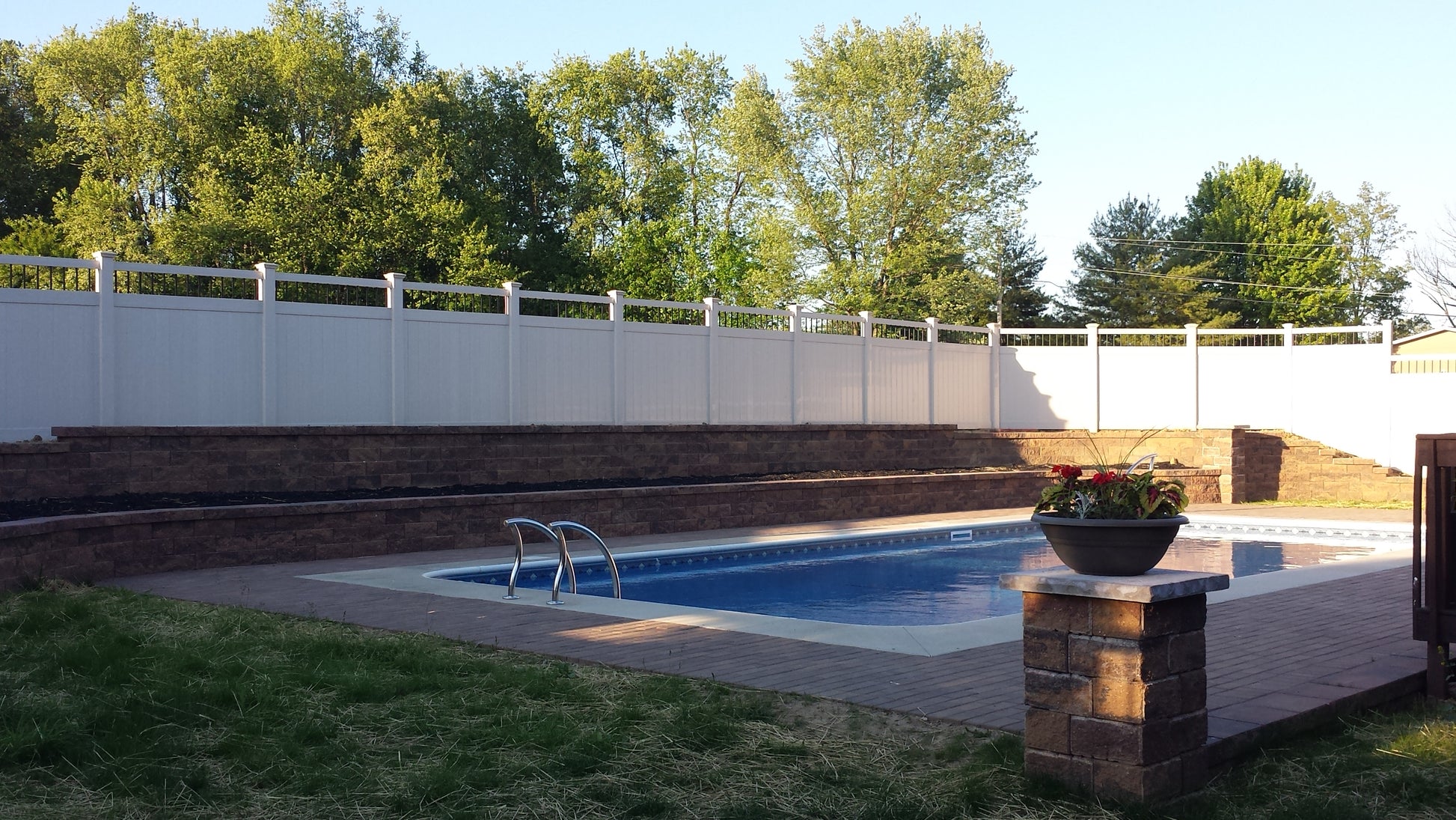 Pool area with a Weatherables Bradford white vinyl privacy fence, trees, and a potted plant.
