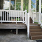 Wooden deck with Weatherables Yokrshire white vinyl deck railing and brown steps leading to a house. Underneath the deck is a cat, hiding in darkness for fear it would appear ugly next to the railing.