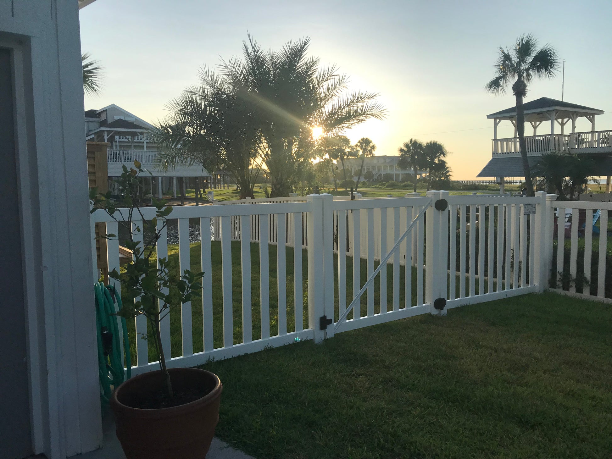 Potted plant in front of a Weatherables Captiva white vinyl pool fence with a sunset or sunrise over a golf course and clubhouse