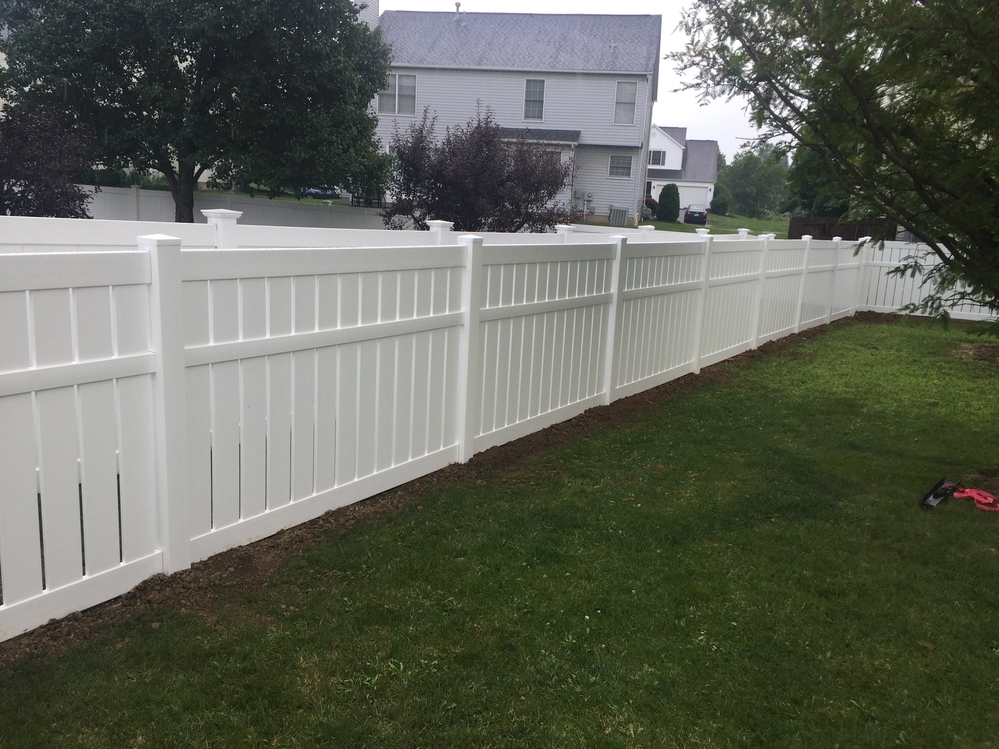 Weatherables Glendale white vinyl semi-privacy fence in a residential backyard with a house and trees in the background.