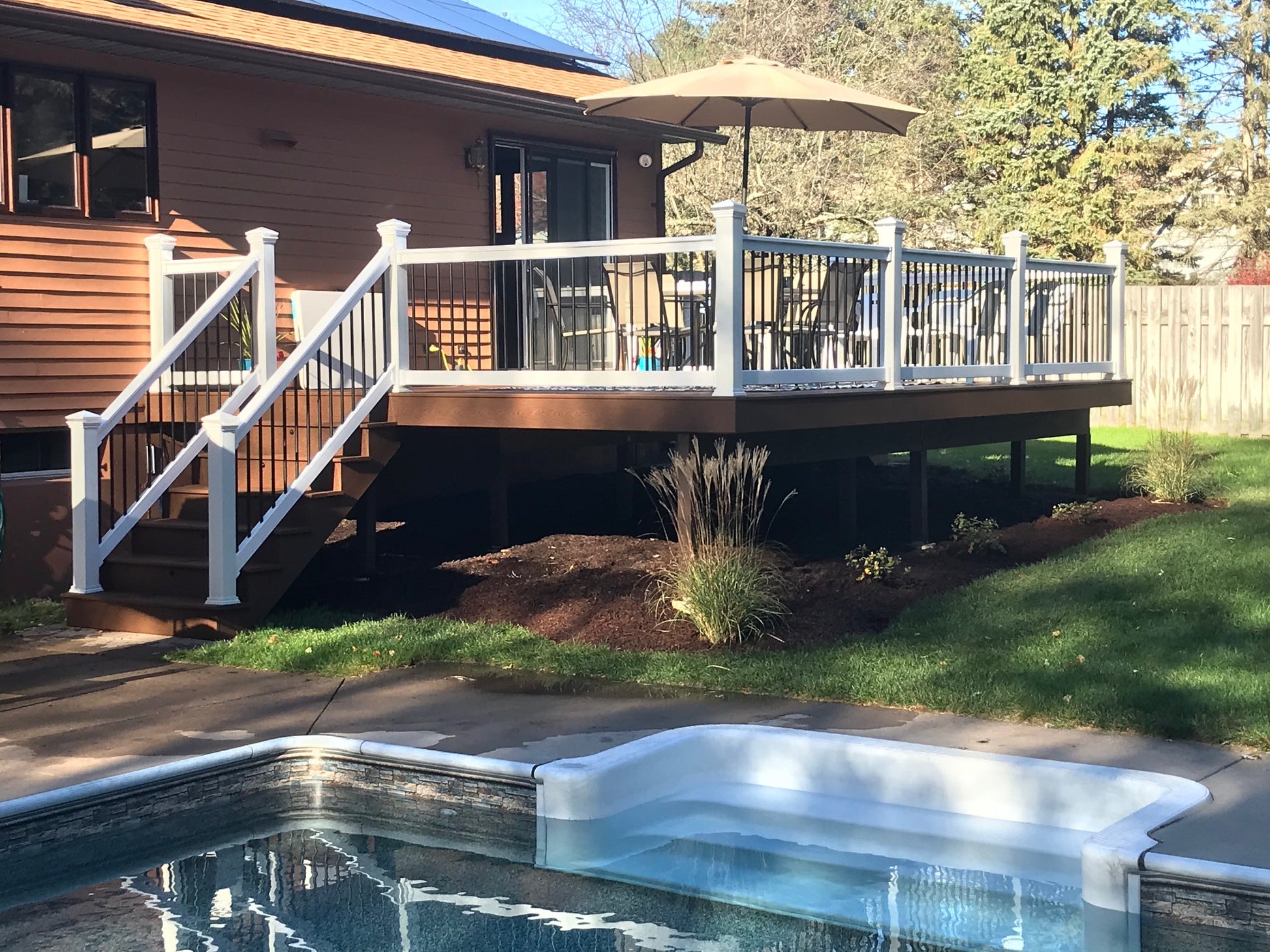 Backyard with pool, deck, Weatherables Wiltshire white vinyl deck railing and umbrella on a sunny day