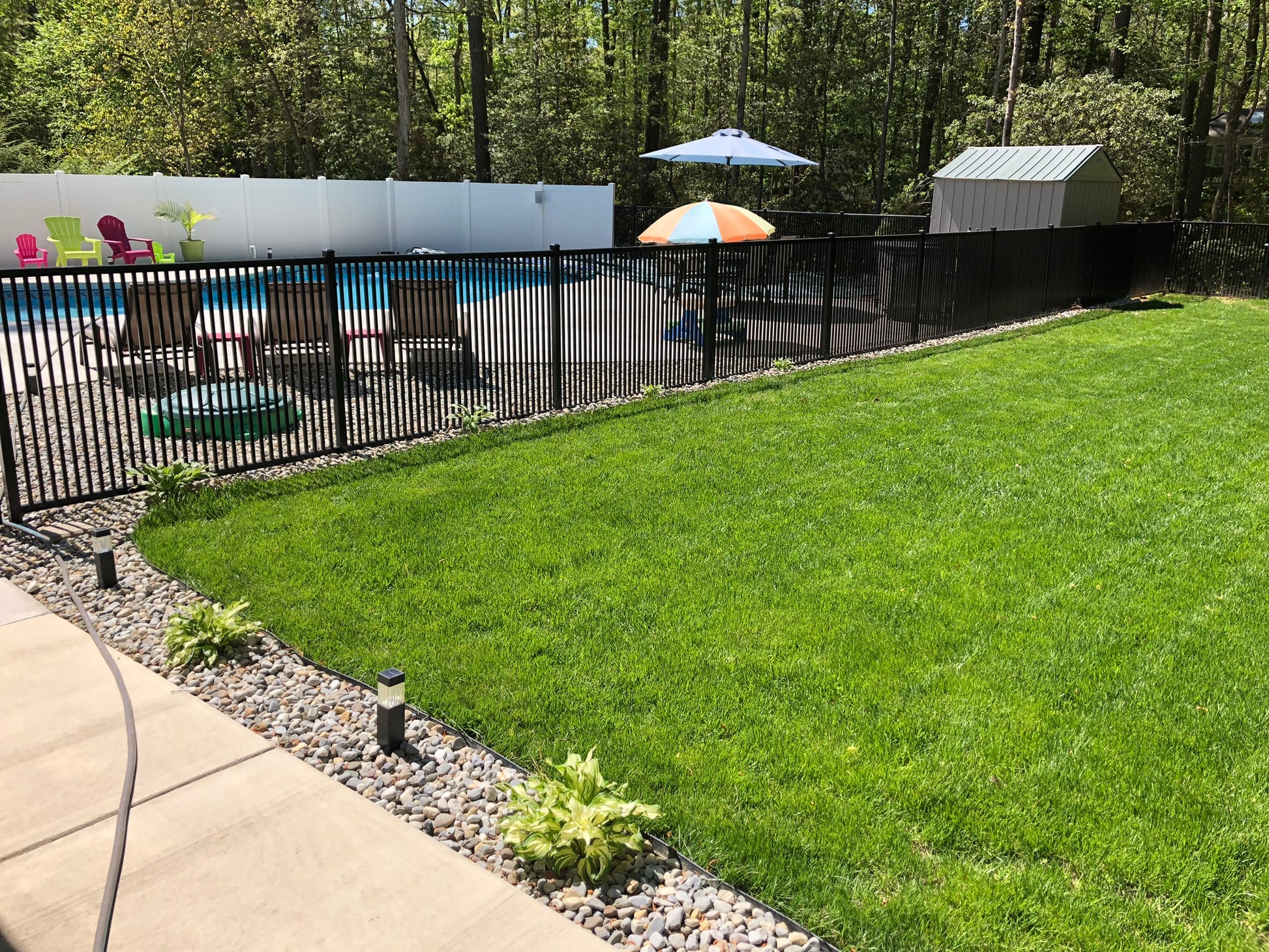 Backyard with Weatherables Atlantic black aluminum fencing, green grass, pool area, and outdoor furniture.