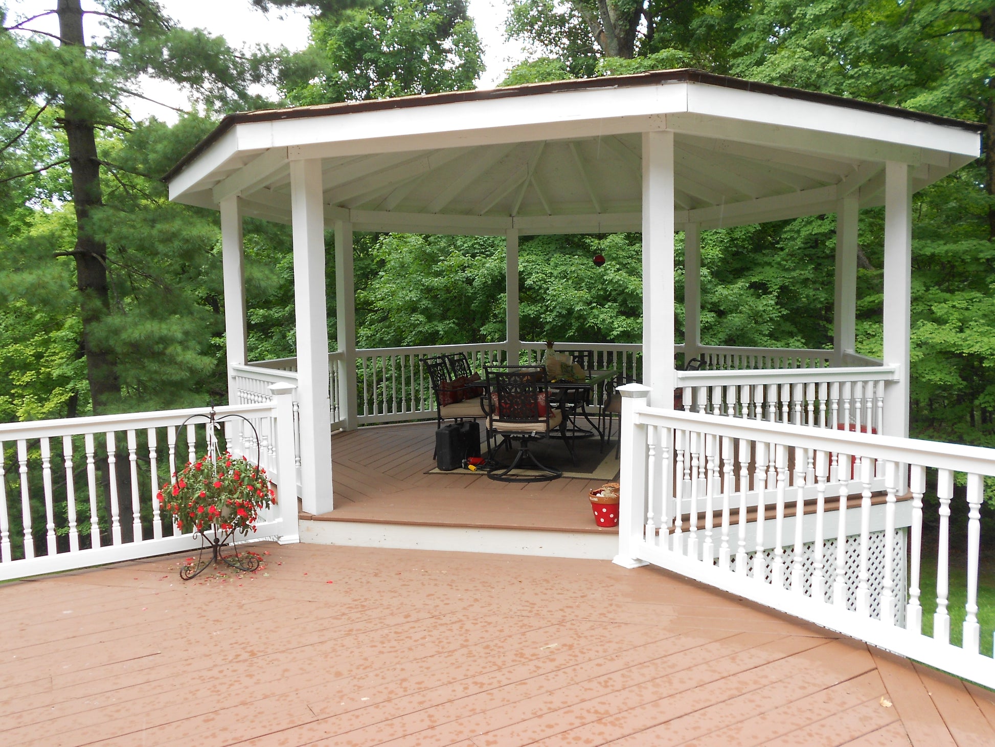 White gazebo on a wooden deck with Weatherables Addison white vinyl deck railing,  chairs and tables, surrounded by trees.