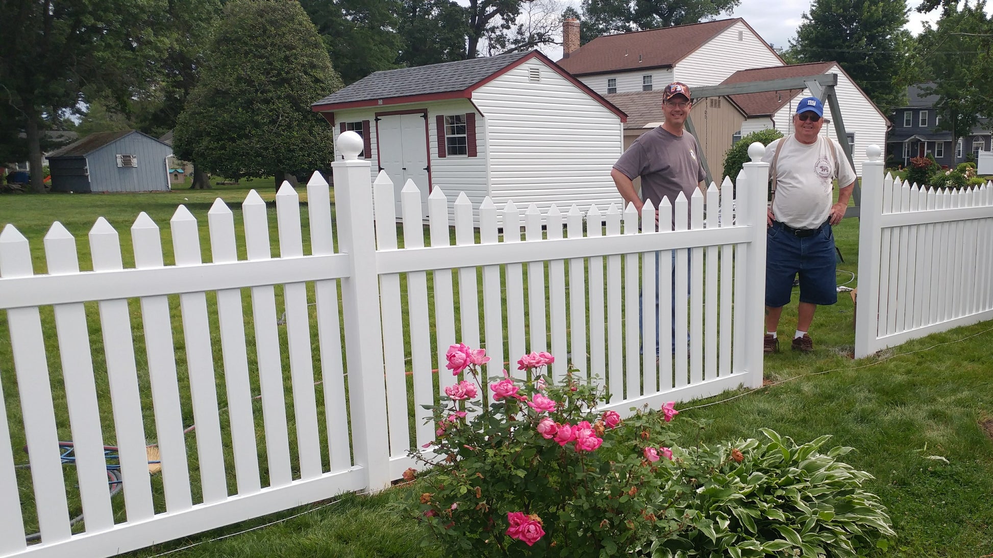 Two men standing behind a Weatherables Hampshire white vinyl picket fence with a small house in the background.