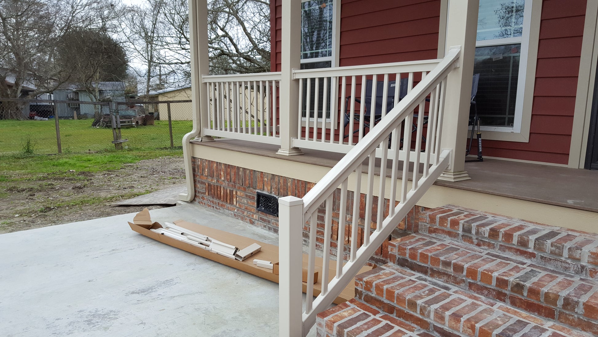 Front porch with Weatherables Yorkshire tan vinyl deck railing and steps leading to a house, with construction materials on the ground.