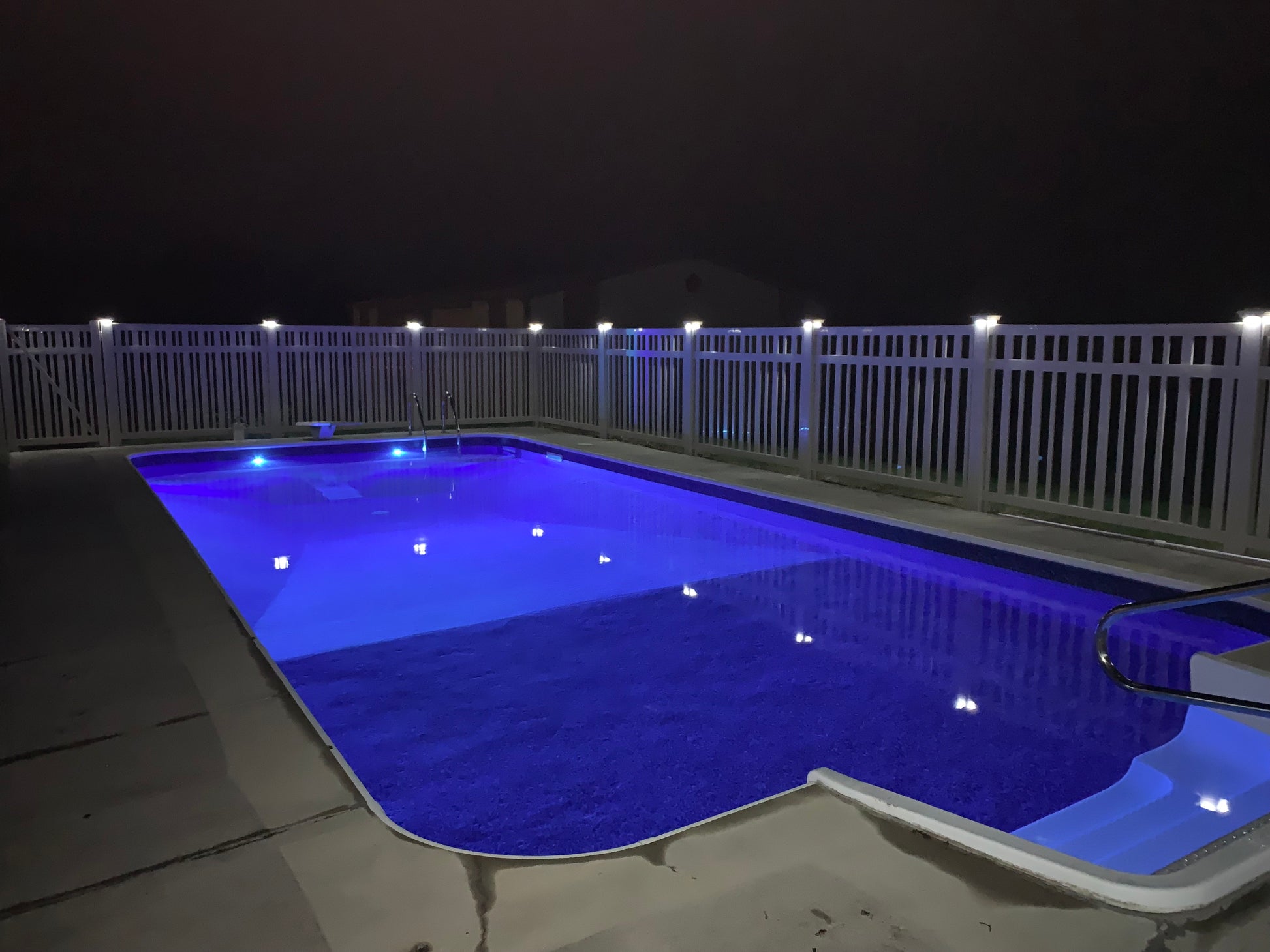 Pool at night with illuminated deck and Weatherables Sarasota white vinyl pool fence and LED lighting post caps