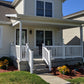 Front porch of a house with Weatherables Berkshire white vinyl patio railings and steps, surrounded by greenery.