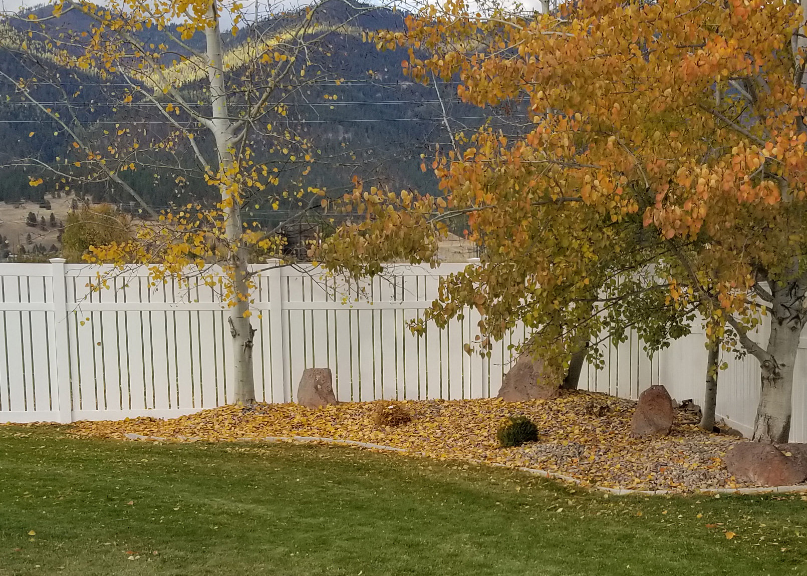 Backyard with trees, rocks, and a Weatherables Alden white vinyl semi-privacy fence in the background